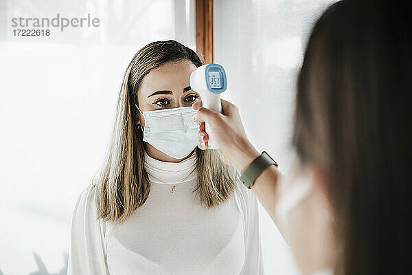 Weiblicher Patient mit Gesichtsschutz  der den Arzt bei der Temperaturkontrolle in der Klinik beobachtet