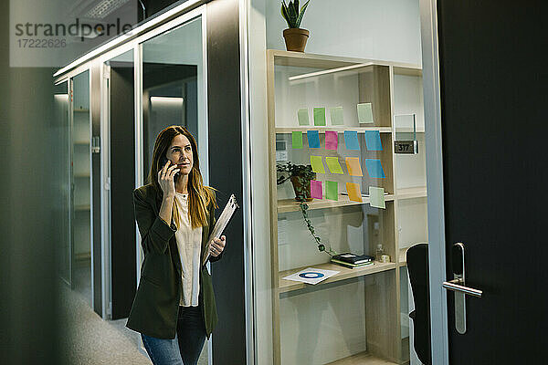 Nachdenkliche Unternehmerin  die im Büro auf dem Flur mit ihrem Smartphone telefoniert