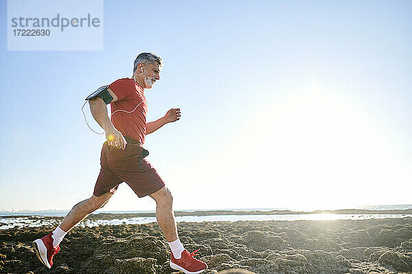 Männlicher Läufer joggt auf Felsen am Strand