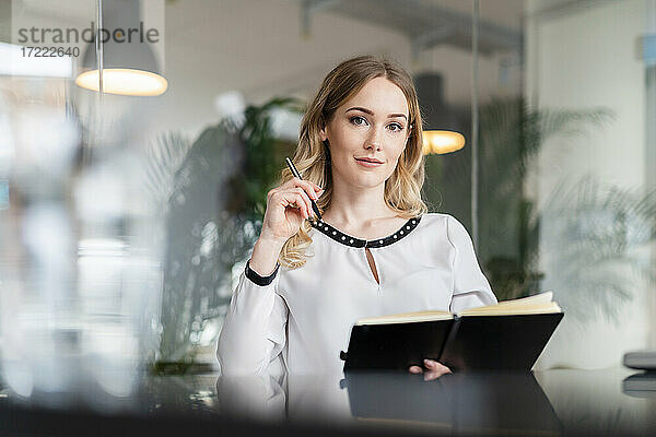 Weibliche Fachkraft mit Tagebuch und Stift sitzt am Schreibtisch im Büro