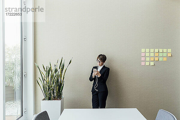 Geschäftsfrau mit In-Ear-Kopfhörern und Mobiltelefon vor einer Wand