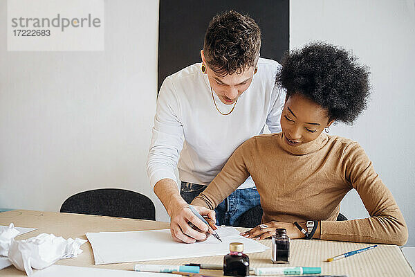 Junger Mann hilft Freundin beim Üben von Kalligraphie im Atelier