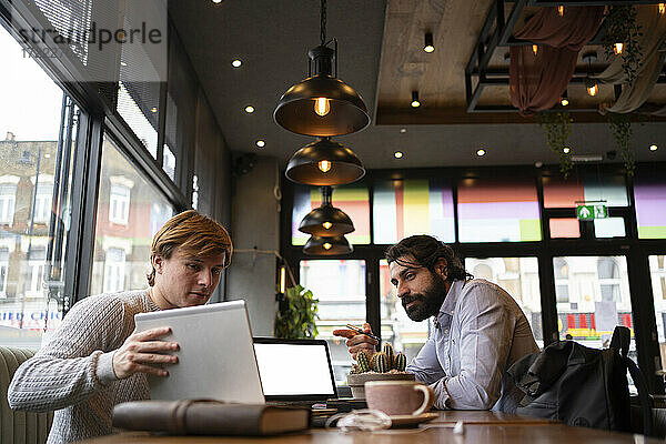 Geschäftsmann zeigt auf den Laptop  den ein Kollege in einem Coworking-Büro hält