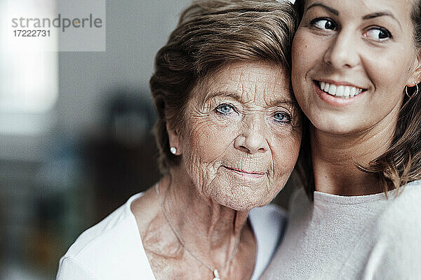 Ältere Frau mit blauen Augen umarmt lächelnde Enkelin zu Hause