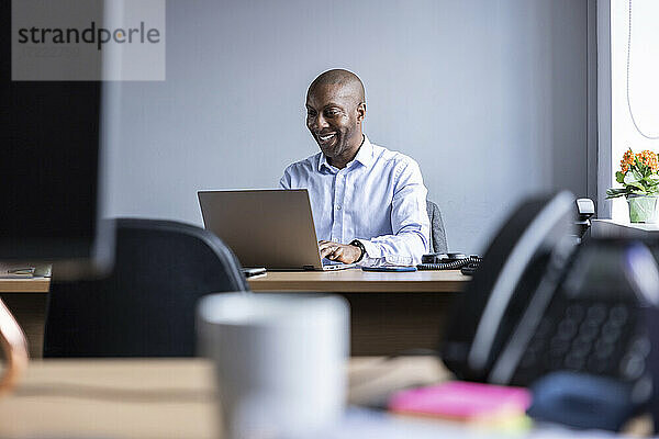 Lächelnder Geschäftsmann mit Laptop bei der Arbeit im Büro