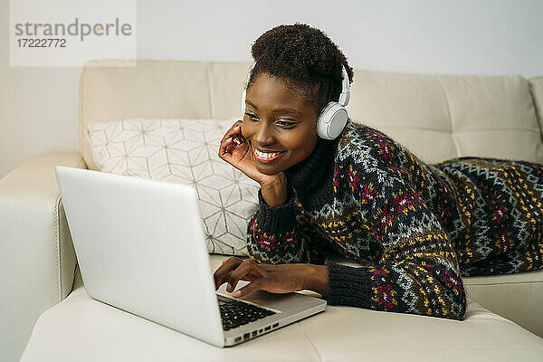 Lächelnde junge Geschäftsfrau  die einen Laptop benutzt und zu Hause Kopfhörer trägt