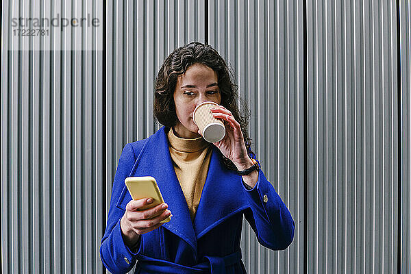 Unternehmerin trinkt Kaffee und benutzt ihr Smartphone vor einer Wand