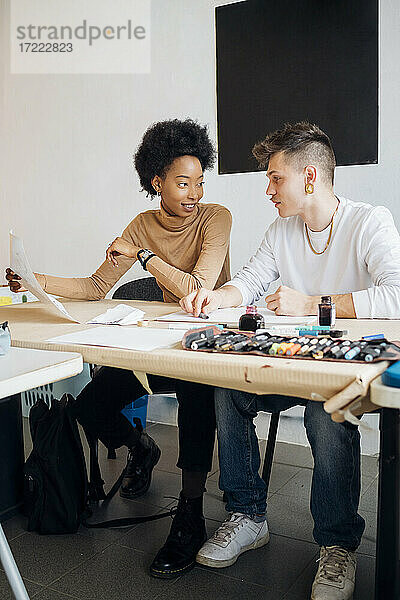 Lächelnde junge Frau im Gespräch mit ihrem Freund  während sie am Tisch im Studio sitzt