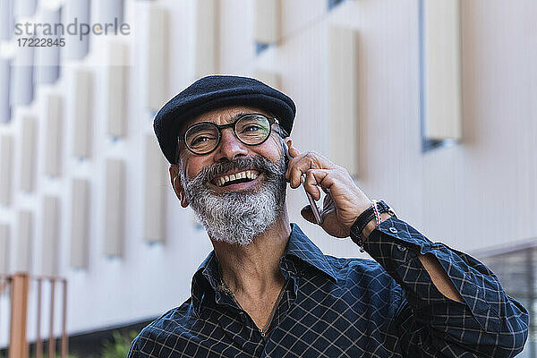 Lächelnder Mann  der wegschaut  während er mit einem Mobiltelefon in der Stadt spricht
