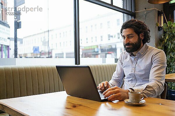 Gut aussehender Geschäftsmann  der einen Laptop benutzt  während er am Schreibtisch im Büro sitzt