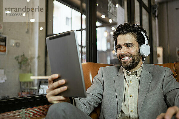 Lächelnder männlicher Unternehmer  der bei einem Videogespräch in einem Café über Kopfhörer zuhört