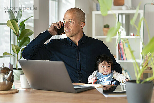 Vater telefoniert mit seinem Smartphone  während er sein kleines Mädchen zu Hause hält