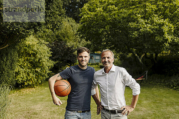 Sohn hält Basketball  während er neben seinem Vater im Hinterhof steht