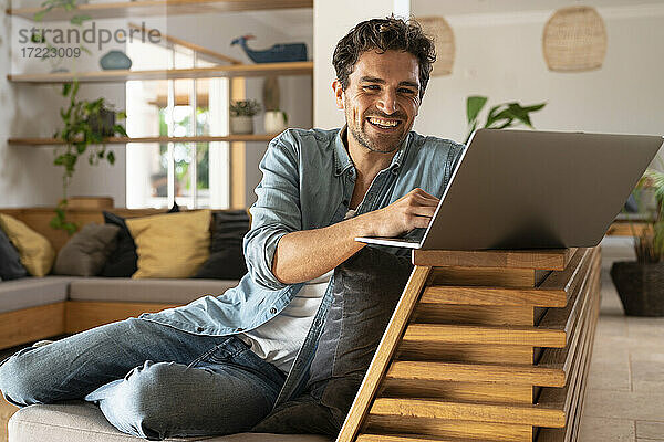 Glücklicher männlicher Freiberufler  der einen Laptop benutzt  während er zu Hause sitzt