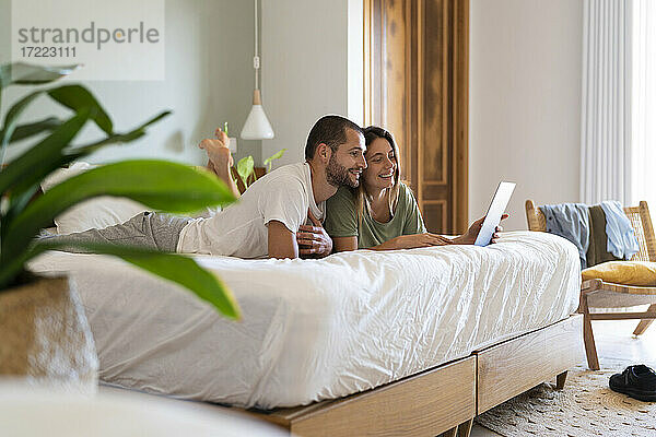 Junges Paar  das einen Laptop benutzt  während es zu Hause im Schlafzimmer auf dem Bett liegt