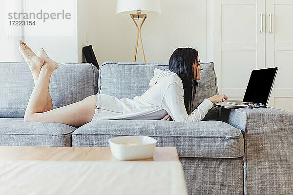 Glückliche Geschäftsfrau  die auf dem Sofa liegt und einen Laptop bei der Arbeit von zu Hause aus benutzt