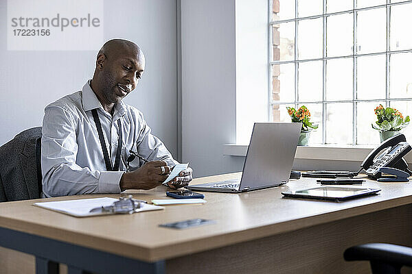 Älterer Geschäftsmann schreibt auf Haftnotiz am Laptop auf dem Schreibtisch im Büro