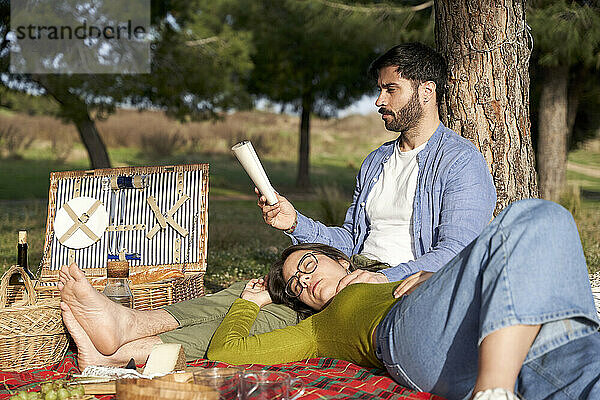 Frau entspannt sich  während ihr Freund beim Picknick auf einer Decke ein Buch liest