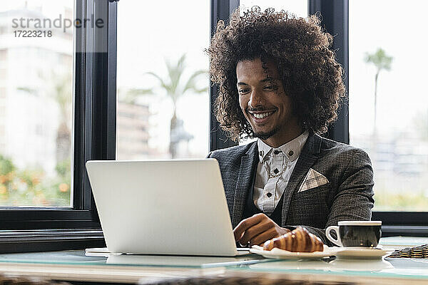 Lächelnder männlicher Jungunternehmer  der in einem Café an einem Laptop arbeitet
