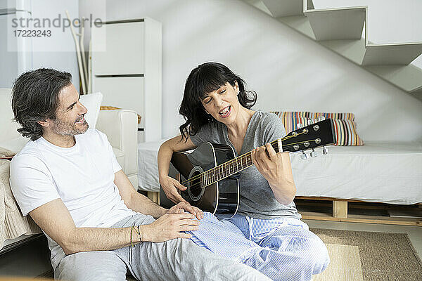 Reifer Mann sieht Frau beim Gitarrenspielen zu Hause an