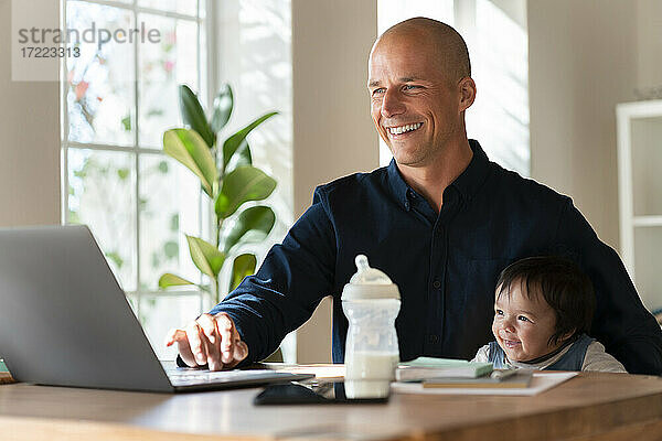 Glücklicher Vater und Tochter schauen auf den Laptop  während sie im Büro zu Hause arbeiten