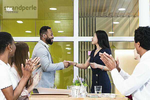 Kollegen klatschen für Unternehmer beim Händeschütteln in einer Sitzung im Büro