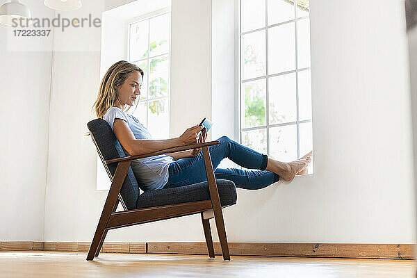 Mittlere erwachsene Frau  die ein digitales Tablet benutzt  während sie zu Hause auf einem Sessel sitzt