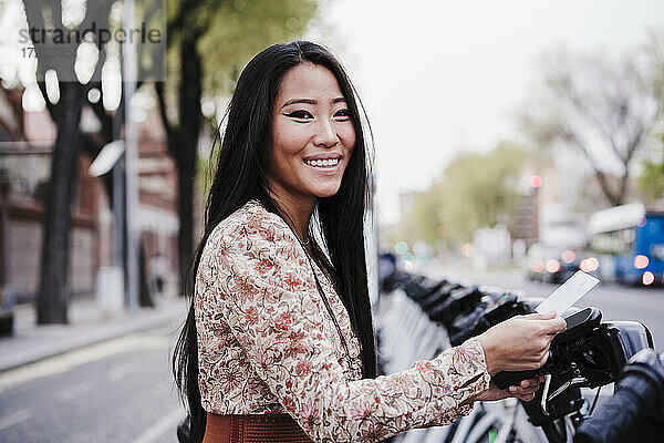Lächelnde Frau  die in der Stadt mit Kreditkarte ein Fahrrad mietet