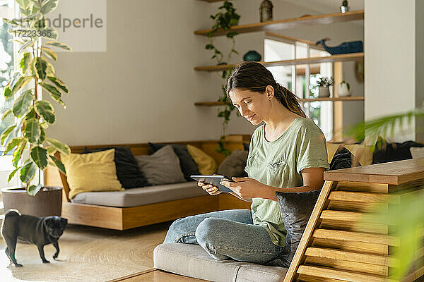 Junge Frau benutzt ein digitales Tablet  während sie zu Hause auf dem Sofa sitzt