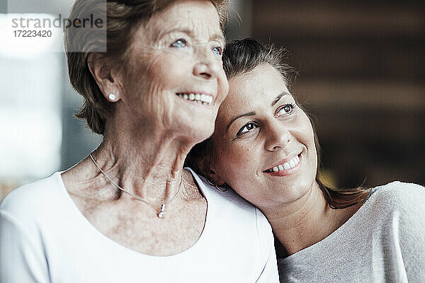 Lächelnde junge Frau und Großmutter träumen  während sie zu Hause wegschauen