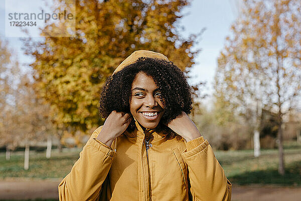 Lächelnde junge Frau  die wegschaut  während sie an einem sonnigen Tag im Park steht