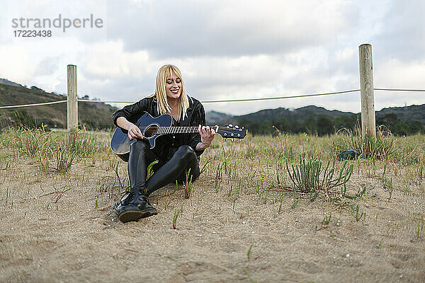 Schöne Frau spielt Gitarre  während sie auf Sand sitzt