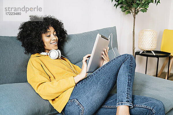 Entspannte junge Frau  die ein digitales Tablet benutzt  während sie zu Hause auf dem Sofa sitzt