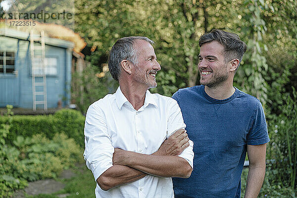 Vater mit verschränkten Armen schaut seinen Sohn an  während er im Garten steht