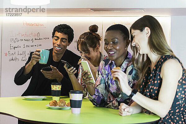 Multiethnische Kollegen lachen bei der Benutzung eines Smartphones im Büro
