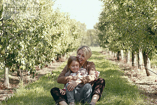 Glückliche Mutter mit Tochter im Gras sitzend im Obstgarten