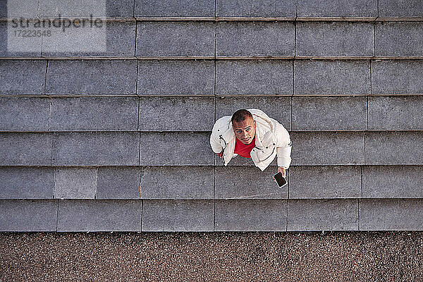 Junger Mann hält Smartphone  während er auf einer Treppe steht