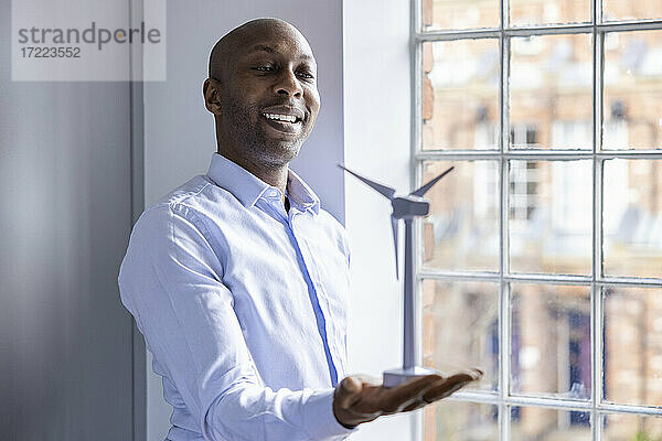 Geschäftsmann  der ein Modell einer Windkraftanlage hält  während er in der Nähe eines Fensters im Büro steht