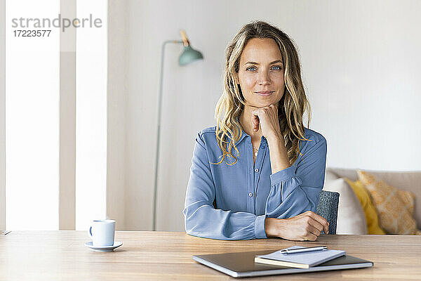 Schöne Geschäftsfrau mit Hand am Kinn sitzt am Schreibtisch im Büro zu Hause