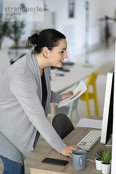 Lächelnde Geschäftsfrau  die einen Desktop-PC bei der Arbeit im Heimbüro benutzt