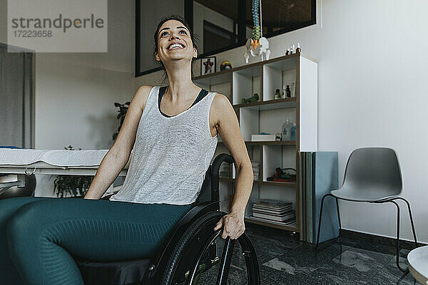 Lächelnde Patientin im Rollstuhl sitzend und wegschauend in einer Arztpraxis