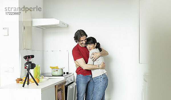 Paar umarmt sich beim Vlogging in der Küche zu Hause