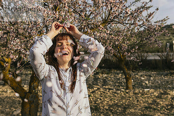 Junge Frau lacht  während sie einen Mandelbaumzweig hält
