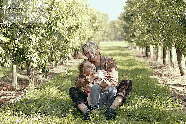 Lächelnde Mutter und Tochter entspannen sich im Obstgarten