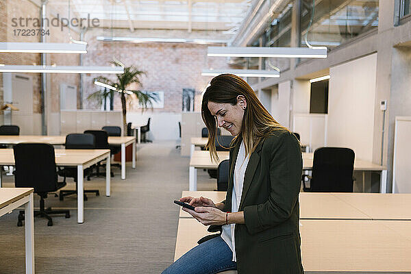 Geschäftsfrau  die ein Smartphone benutzt  während sie auf dem Schreibtisch im Büro sitzt