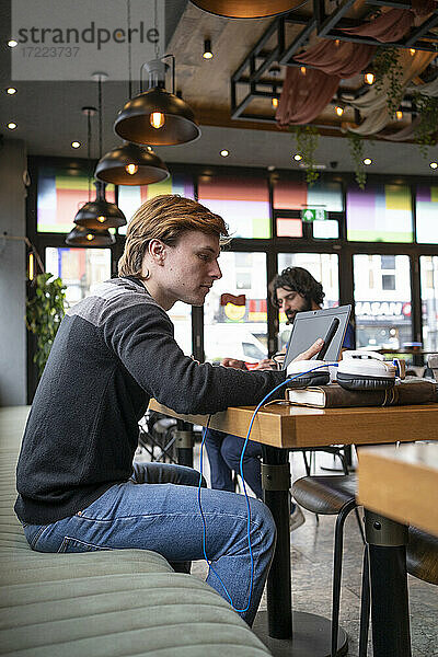 Männlicher Unternehmer sitzt am Schreibtisch und benutzt sein Smartphone in einem Coworking-Büro