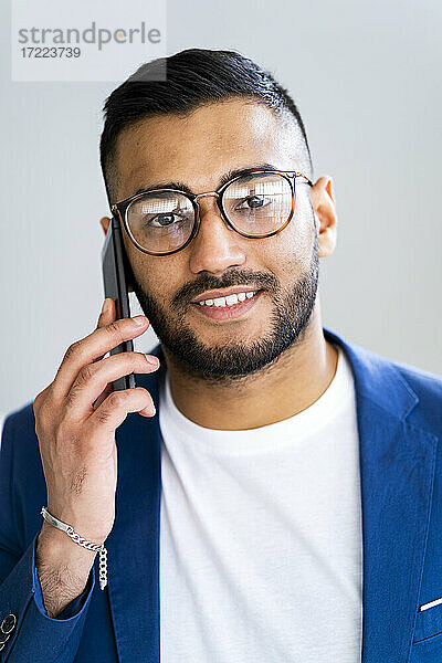 Geschäftsmann mit Brille im Gespräch mit Smartphone an der Wand im Büro