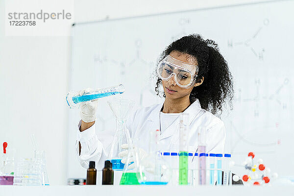 Junge Forscherin gießt bei der Arbeit im Labor Flüssigkeit in einen Kolben