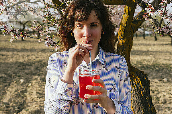 Junge Frau trinkt Erdbeerlimonade am Mandelbaum