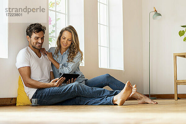Lächelndes Paar  das ein digitales Tablet benutzt  während es zu Hause auf dem Boden sitzt